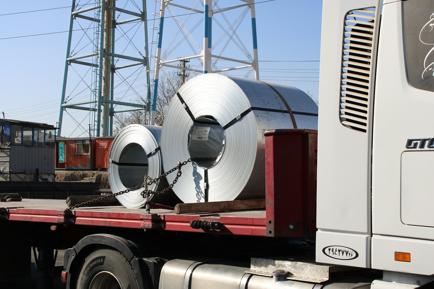 Dwie duże metalowe cewki leżą na zaparkowanej ciężarówce z płaską platformą.